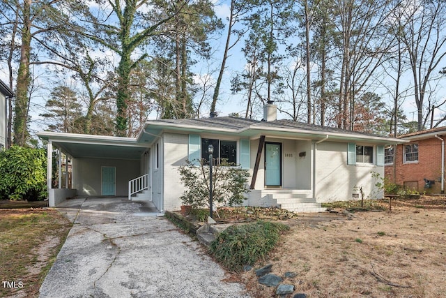 ranch-style house featuring driveway, a chimney, an attached carport, and brick siding