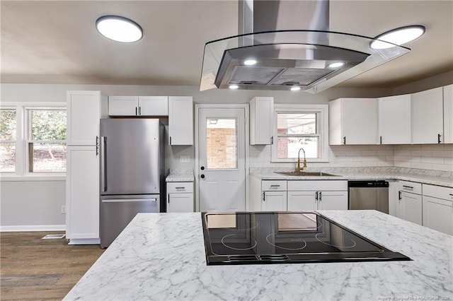 kitchen with stainless steel appliances, a sink, white cabinets, backsplash, and light stone countertops