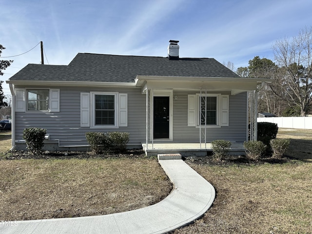 bungalow-style house featuring covered porch, roof with shingles, a chimney, and a front yard