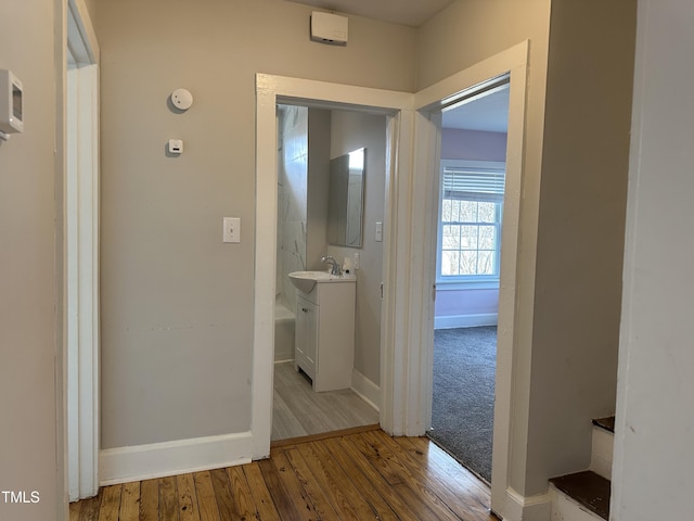 hallway with light wood finished floors, baseboards, and a sink