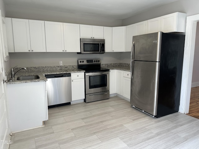 kitchen featuring appliances with stainless steel finishes, a sink, white cabinetry, and light stone countertops