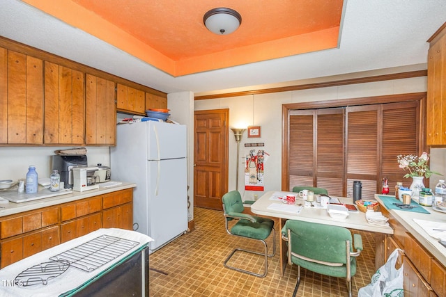 kitchen with light countertops, brown cabinetry, a raised ceiling, and freestanding refrigerator