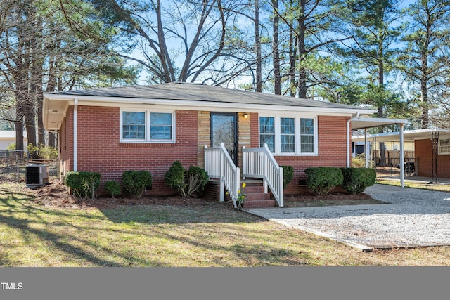 view of front of home featuring brick siding, an attached carport, gravel driveway, cooling unit, and a front yard