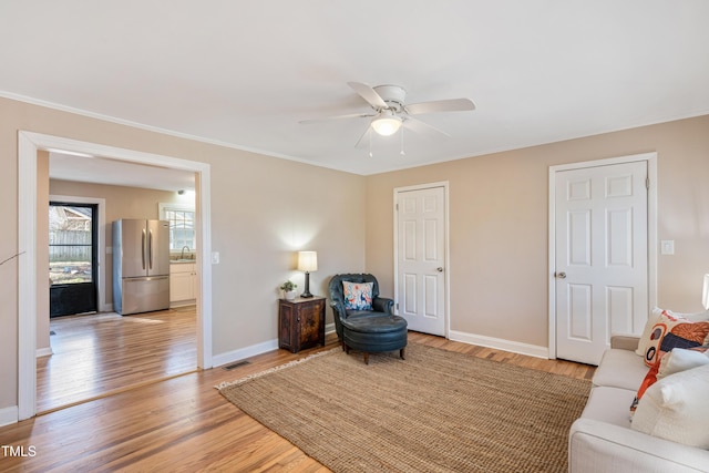 sitting room with visible vents, a ceiling fan, ornamental molding, light wood-type flooring, and baseboards