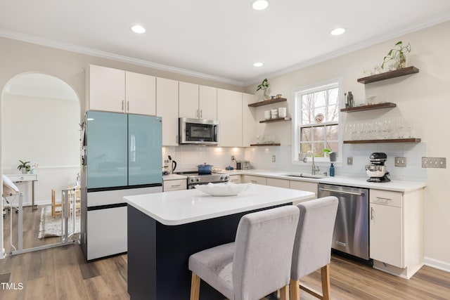 kitchen featuring a sink, open shelves, ornamental molding, and stainless steel appliances