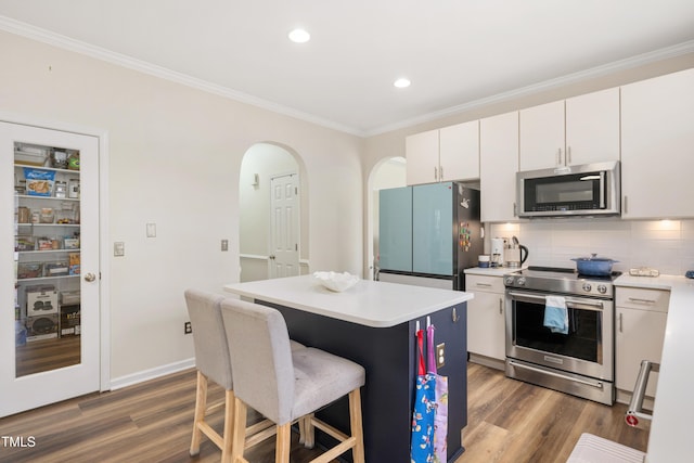 kitchen featuring crown molding, decorative backsplash, appliances with stainless steel finishes, wood finished floors, and arched walkways