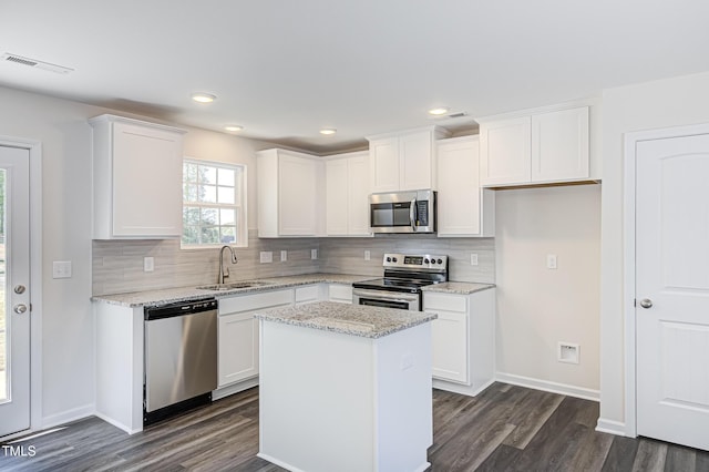 kitchen featuring light stone counters, a kitchen island, a sink, white cabinets, and appliances with stainless steel finishes