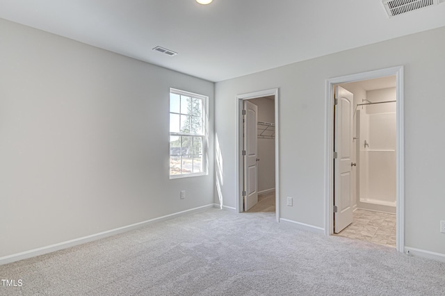 unfurnished bedroom with baseboards, a spacious closet, visible vents, and light colored carpet