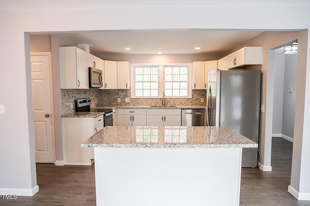 kitchen featuring stainless steel appliances, white cabinetry, light stone countertops, and a center island