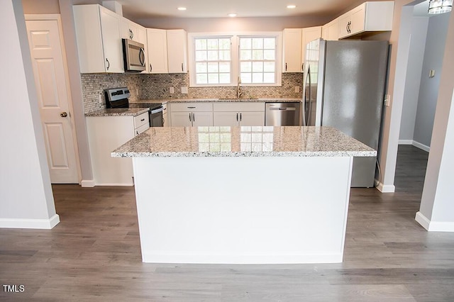 kitchen featuring a kitchen island, white cabinetry, stainless steel appliances, and light stone counters