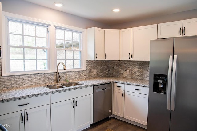 kitchen with stainless steel appliances, light stone counters, a sink, and white cabinets