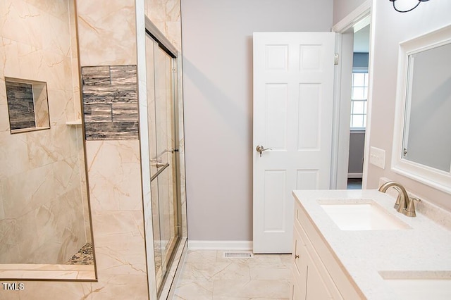 bathroom with marble finish floor, double vanity, a sink, a shower stall, and baseboards