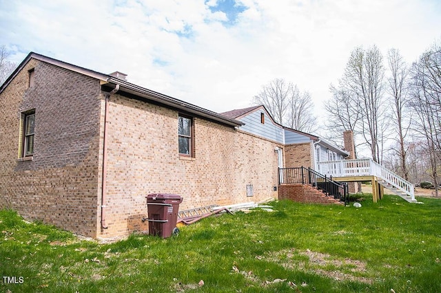 view of side of home with brick siding, a yard, stairway, and a wooden deck