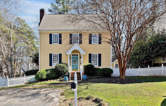 colonial inspired home with fence, a chimney, and a front lawn