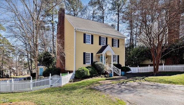 colonial-style house with a fenced front yard, a front yard, and a chimney