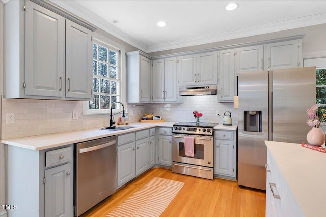 kitchen featuring stainless steel appliances, light countertops, ornamental molding, a sink, and under cabinet range hood