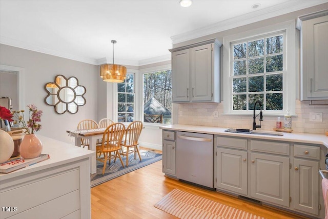 kitchen featuring pendant lighting, light countertops, stainless steel dishwasher, ornamental molding, and a sink