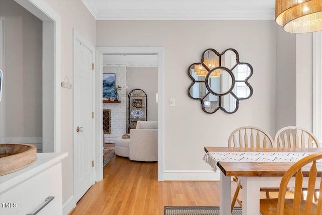 dining room featuring light wood finished floors, baseboards, a fireplace, and ornamental molding