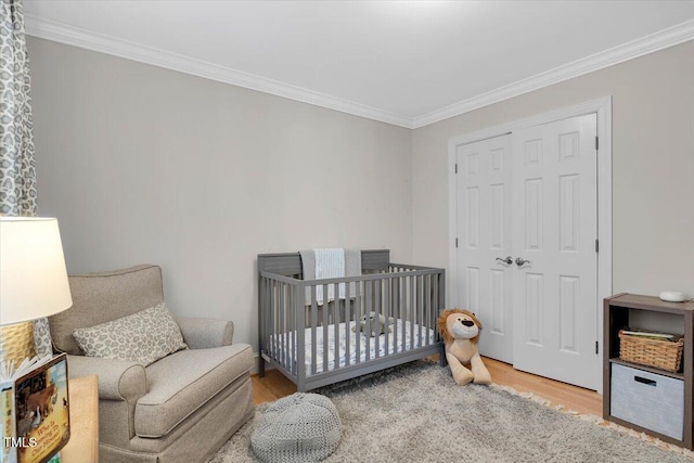 bedroom with a nursery area, crown molding, and wood finished floors