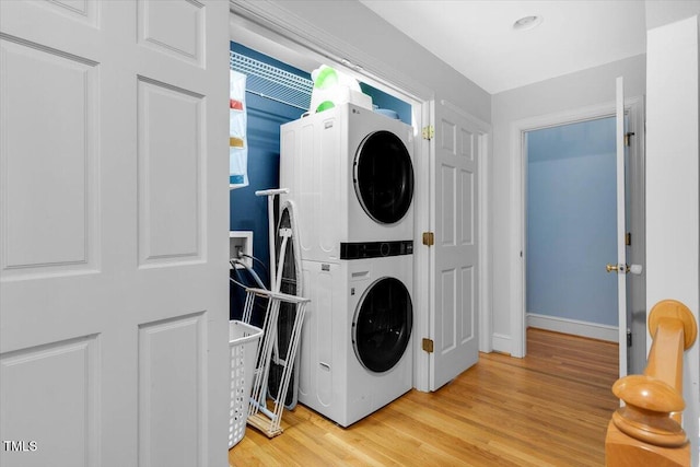 washroom with stacked washer / dryer, laundry area, baseboards, and wood finished floors