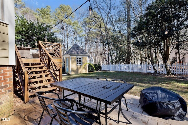 view of patio with a storage shed, a fenced backyard, stairway, an outbuilding, and outdoor dining area