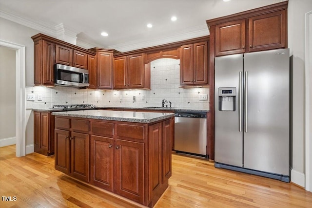 kitchen with light wood finished floors, decorative backsplash, appliances with stainless steel finishes, a sink, and a kitchen island