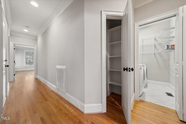 corridor with light wood-type flooring, ornamental molding, independent washer and dryer, and visible vents