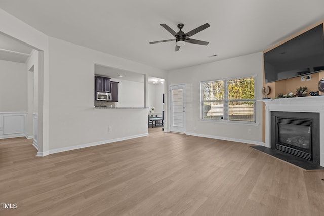 unfurnished living room featuring light wood-style floors, a fireplace with flush hearth, baseboards, and ceiling fan