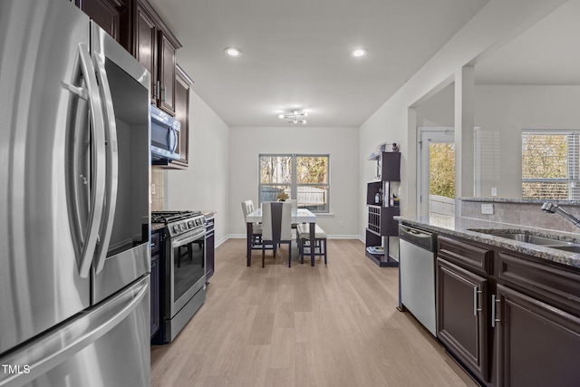 kitchen featuring light wood finished floors, a wealth of natural light, appliances with stainless steel finishes, stone countertops, and dark brown cabinetry