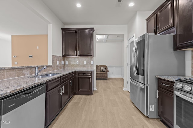 kitchen featuring light stone counters, stainless steel appliances, a sink, visible vents, and light wood-type flooring