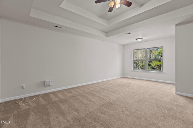 spare room featuring a ceiling fan, visible vents, baseboards, a tray ceiling, and carpet