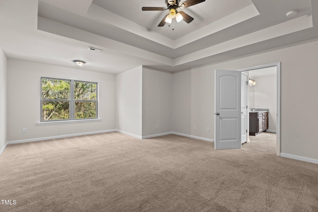 spare room with light carpet, a tray ceiling, visible vents, and baseboards