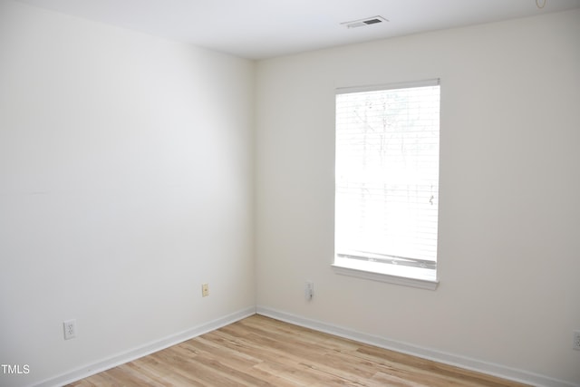 spare room with light wood-type flooring, visible vents, and baseboards