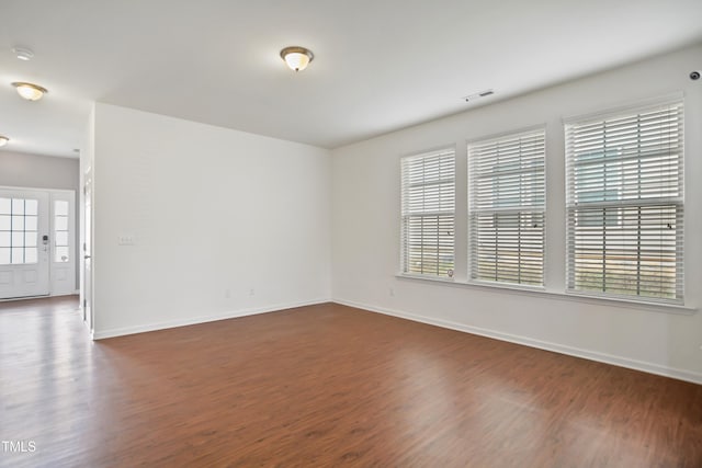 empty room with dark wood-style floors, visible vents, and baseboards