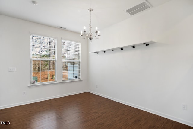 empty room with a notable chandelier, dark wood finished floors, visible vents, and baseboards