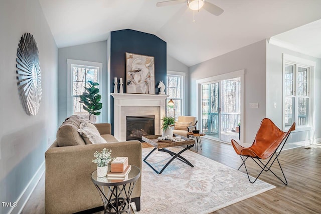 living room with a ceiling fan, a glass covered fireplace, vaulted ceiling, wood finished floors, and baseboards