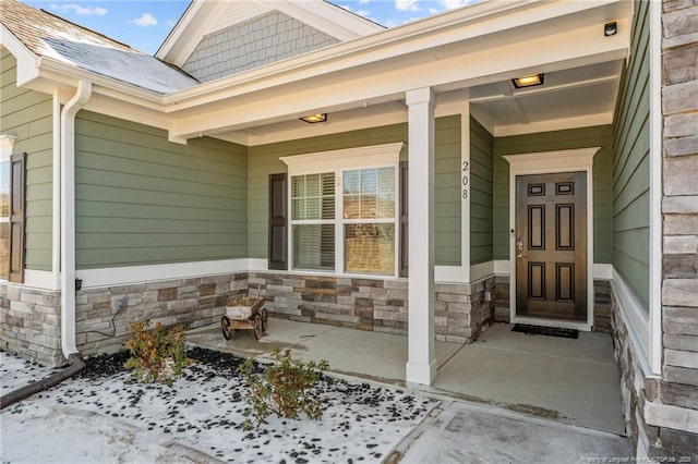 entrance to property featuring stone siding, a shingled roof, and covered porch