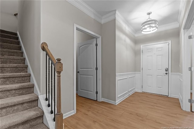 foyer featuring a chandelier, a decorative wall, ornamental molding, wainscoting, and light wood finished floors