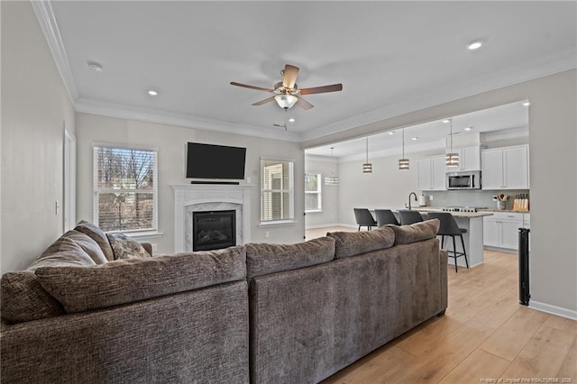 living room featuring recessed lighting, a premium fireplace, a ceiling fan, light wood finished floors, and crown molding