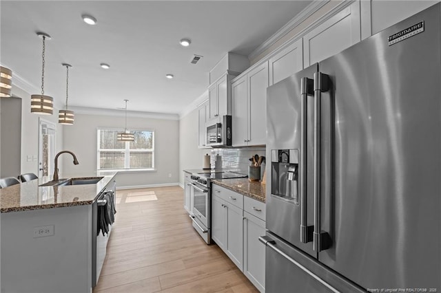 kitchen with appliances with stainless steel finishes, ornamental molding, dark stone countertops, a kitchen island with sink, and pendant lighting