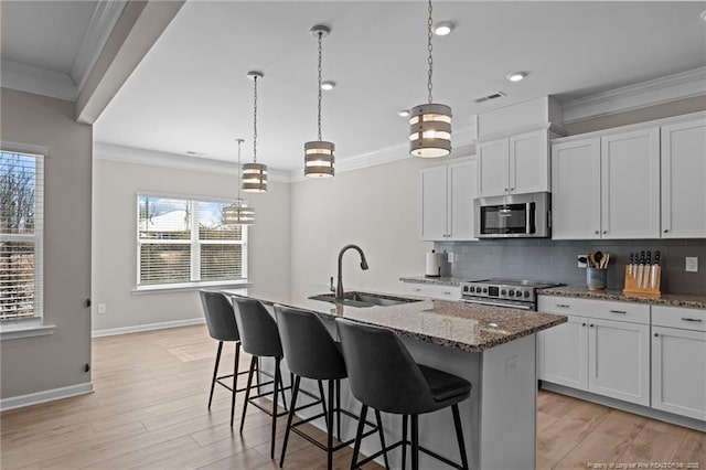 kitchen featuring stainless steel appliances, a sink, white cabinetry, an island with sink, and dark stone countertops