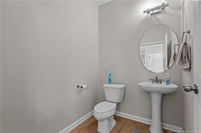 half bathroom featuring toilet, a sink, baseboards, and wood finished floors