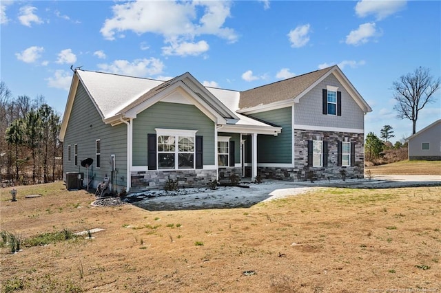 craftsman-style house featuring central air condition unit, stone siding, and a front yard