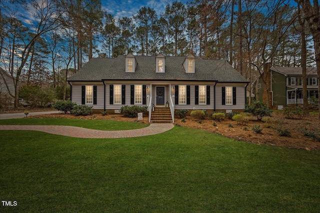 cape cod-style house featuring roof with shingles and a front lawn