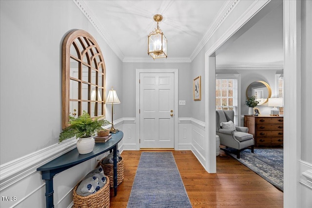 entryway with a decorative wall, crown molding, wood finished floors, wainscoting, and an inviting chandelier