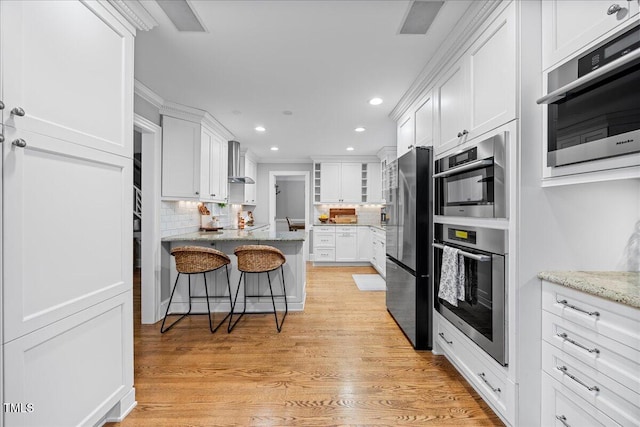 kitchen with freestanding refrigerator, white cabinetry, wall chimney range hood, and a kitchen bar