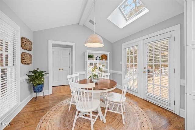 dining space with light wood-type flooring, vaulted ceiling with skylight, french doors, and baseboards