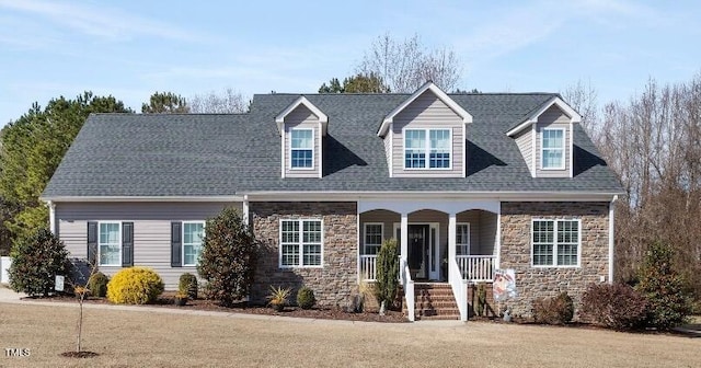 cape cod home with a porch, stone siding, a shingled roof, and a front lawn