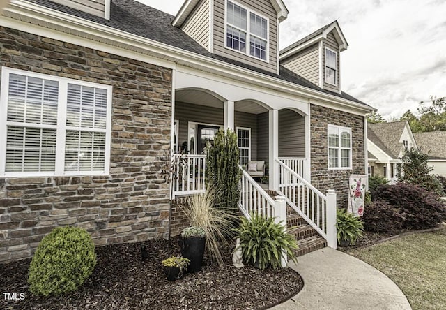 property entrance with roof with shingles, a porch, and stone siding