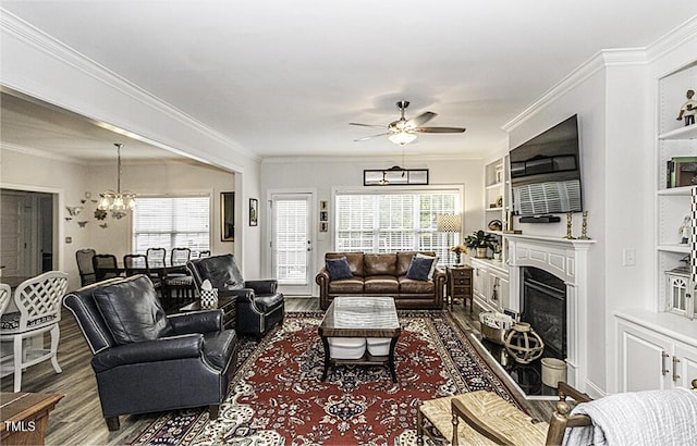 living area with dark wood-type flooring, ceiling fan with notable chandelier, a fireplace, and ornamental molding